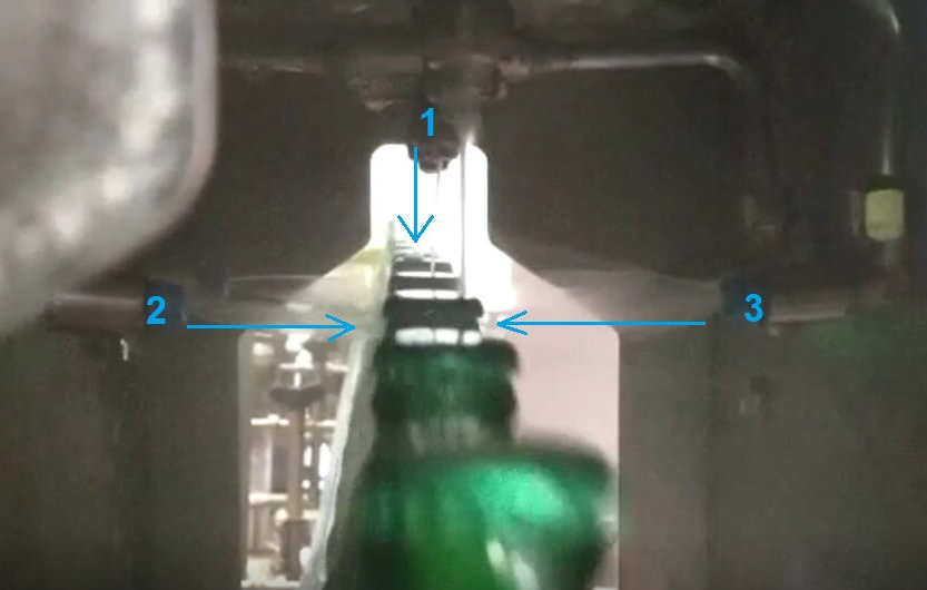 Das Foto zeigt mehrere Bierflaschen in einer industriellen Abfüllanlage. Sprühdüsen übernehmen die Reinigung und Desinfektion der Flaschen.